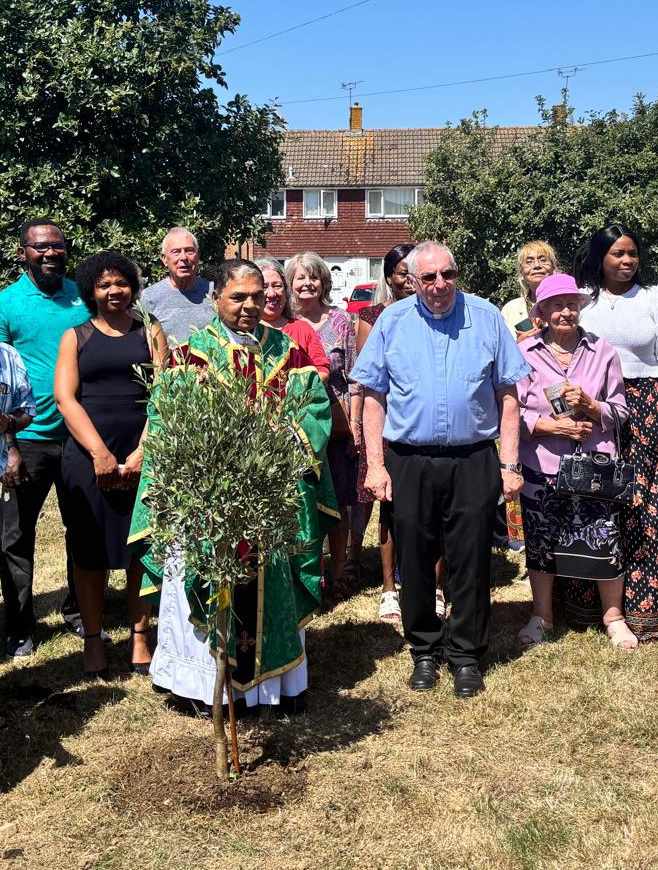 Fr. Jose, parish priest for St. Simon Stock Catholic Church, standing with parishioners next to the commemorative tree to mark his 70th birthday.